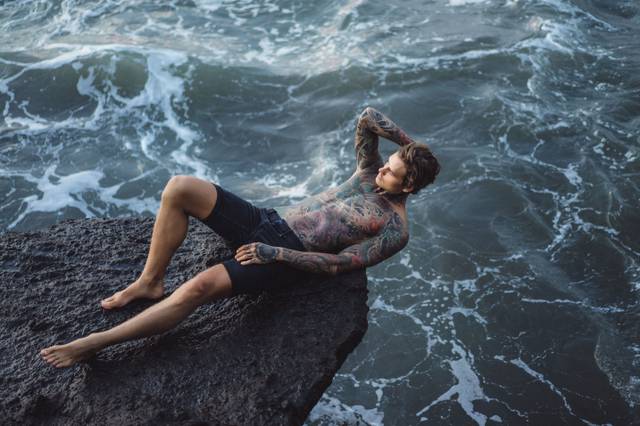 tattooed-man-lies-edge-cliff-splashes-ocean-waves (1).jpg